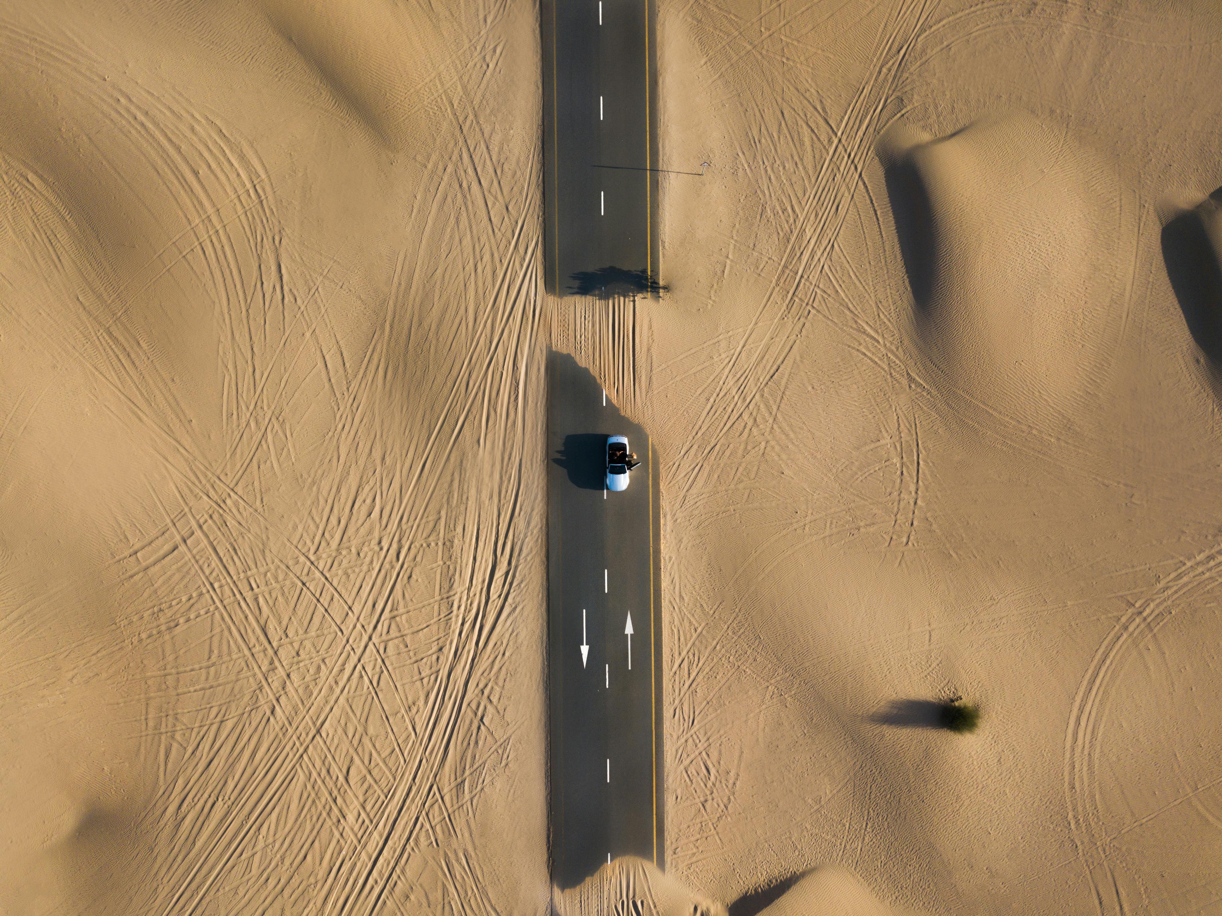 Aerial view of a desert road with a vehicle driving through sand dunes—symbolizing infrastructure challenges and solar lighting needs in harsh Middle Eastern climates.