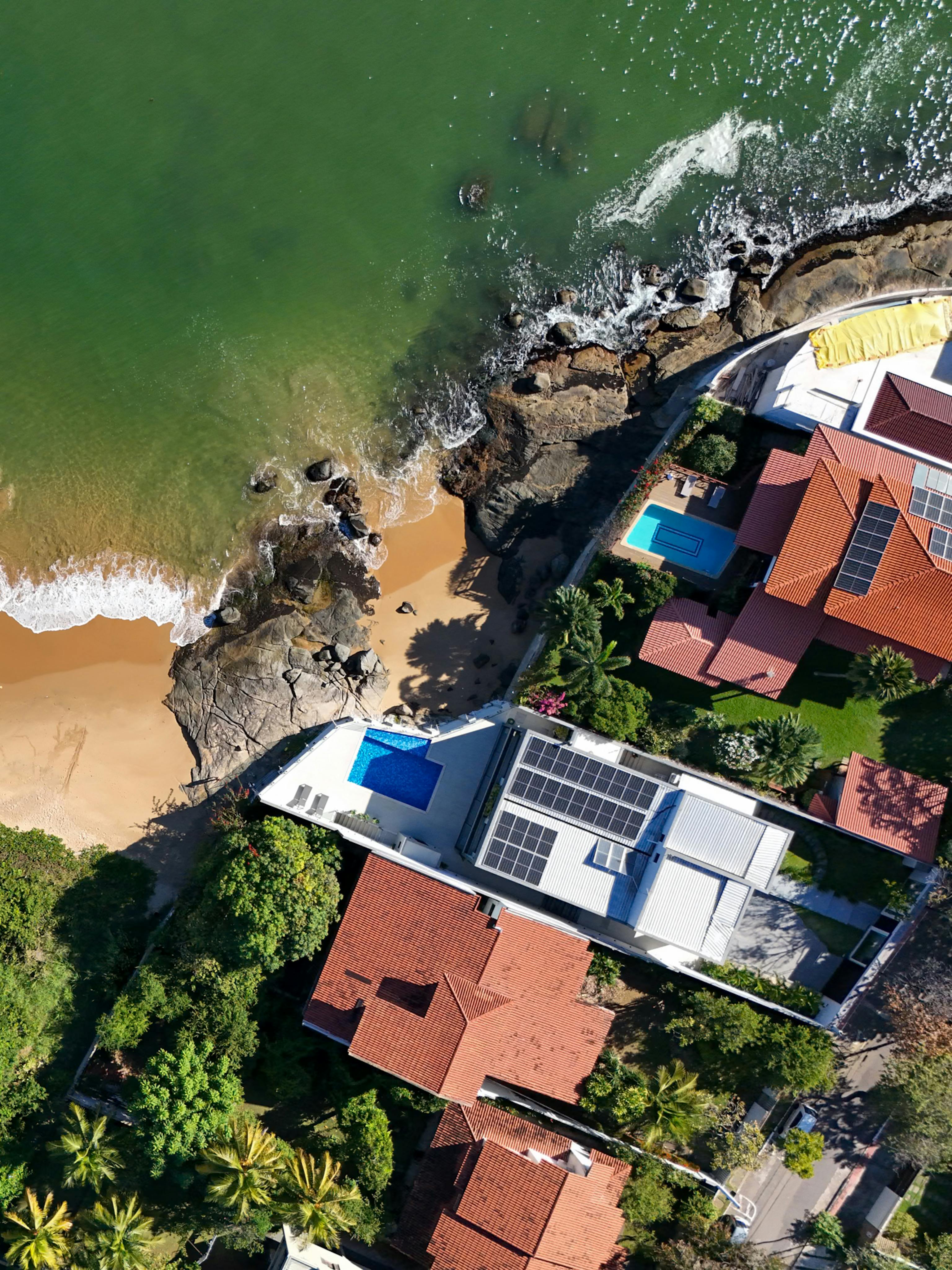 Aerial view of seaside residential villas with rooftop solar panel installations, showcasing sustainable solar adoption in coastal properties.