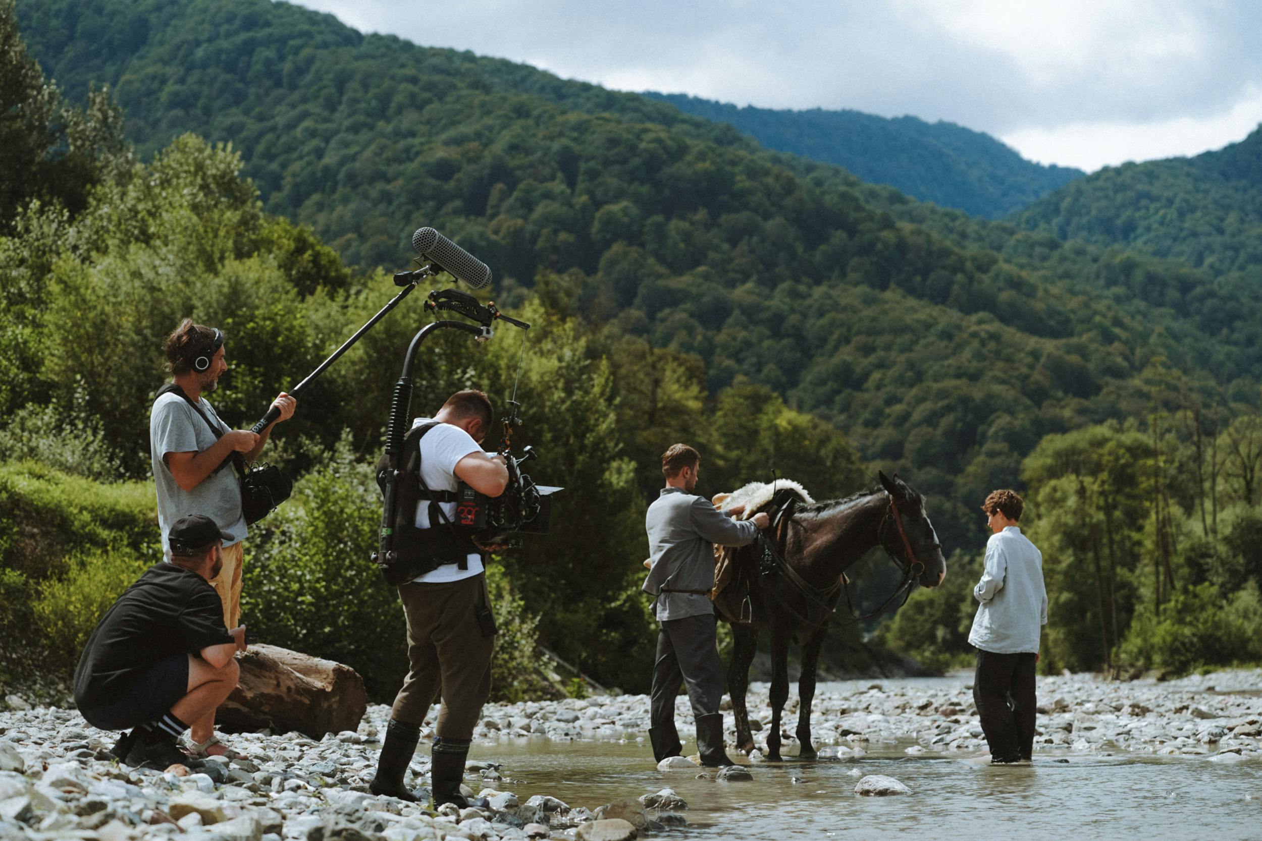 Film crew recording a period scene by a river in remote forest terrain—showcasing a real-world application for Gletscher Energy’s off-grid power stations and portable battery banks for on-location media production.