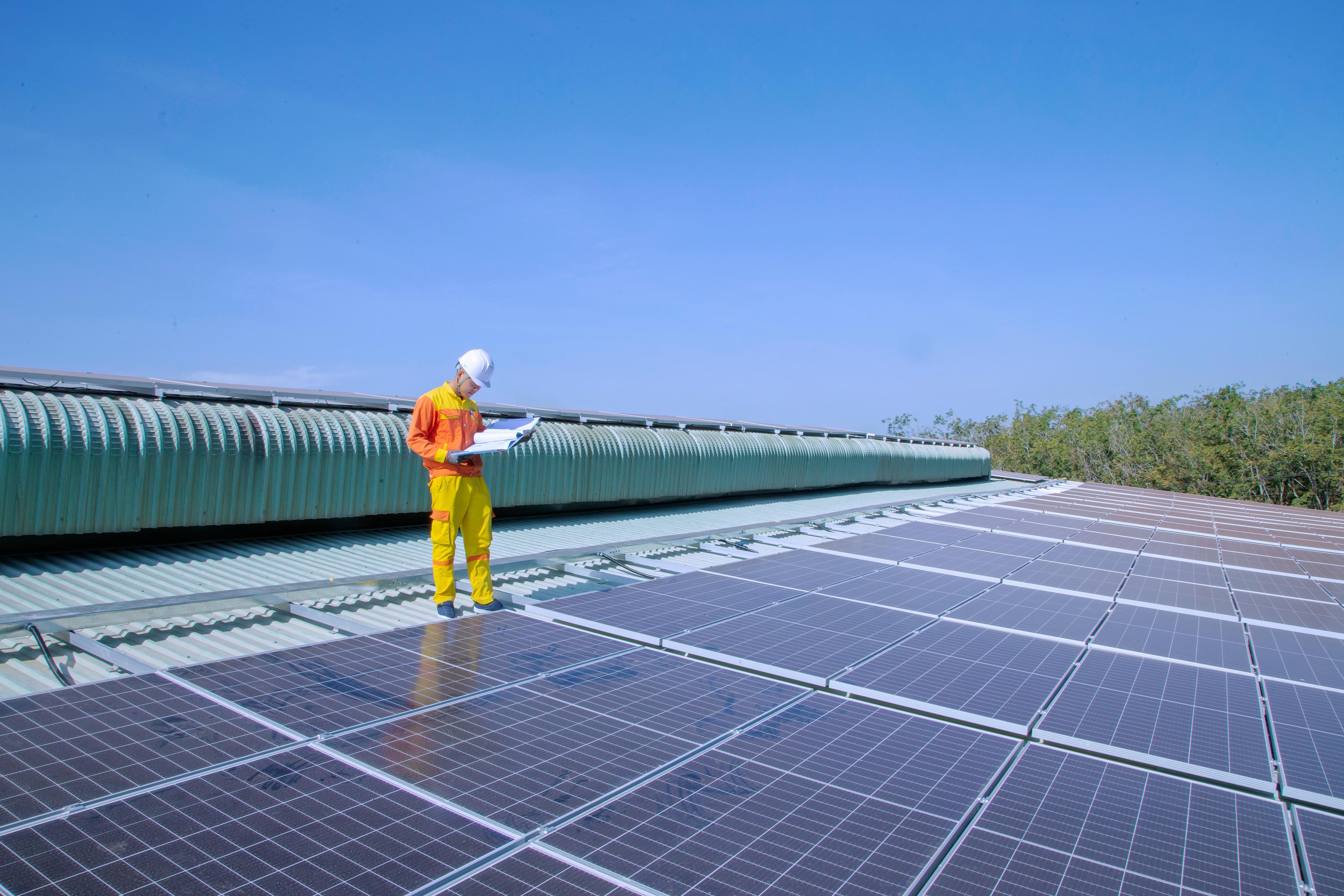 A solar technician performs inspection on industrial rooftop solar panels under clear skies, representing quality control and operational assurance for Gletscher Energy’s Makellos Element Series PV systems.
