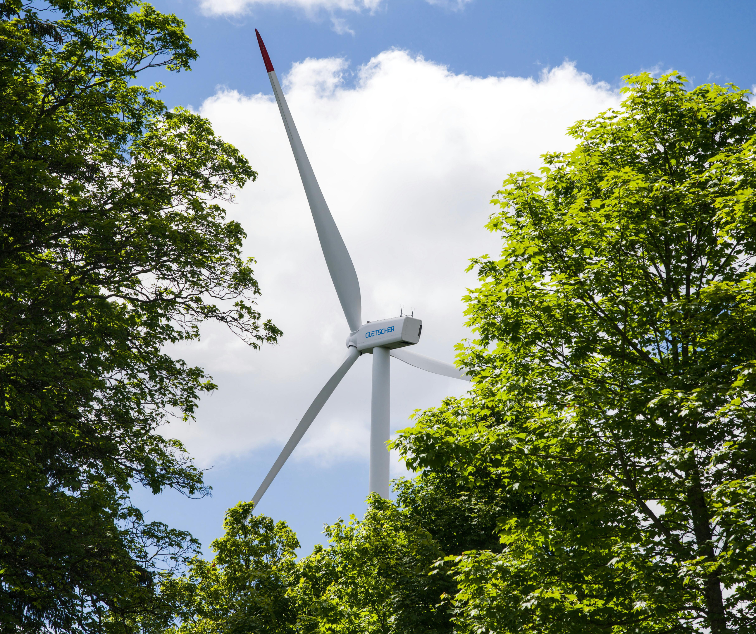 Gletscher-branded wind turbine surrounded by green trees, highlighting clean energy integration with natural landscapes.